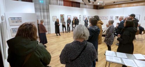 Människor står i en konstutställning och lyssnar på konstnärens berättelse