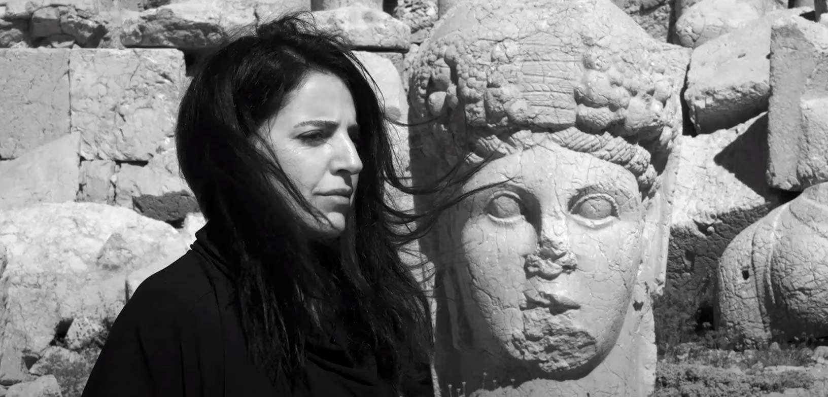 Vinden blåser i Bejan Maturs hår. I bakgrunden en staty