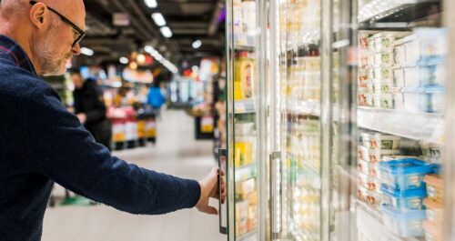 Äldre man öppnar kyldörr i affär