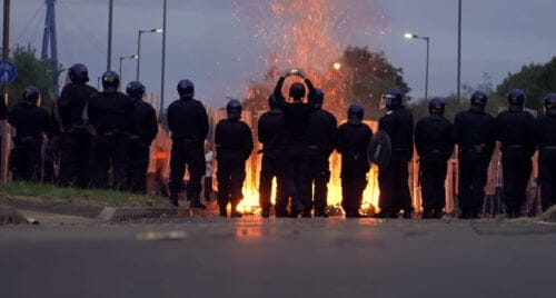 Kravallpoliser står framför en hög med brinnande bråte