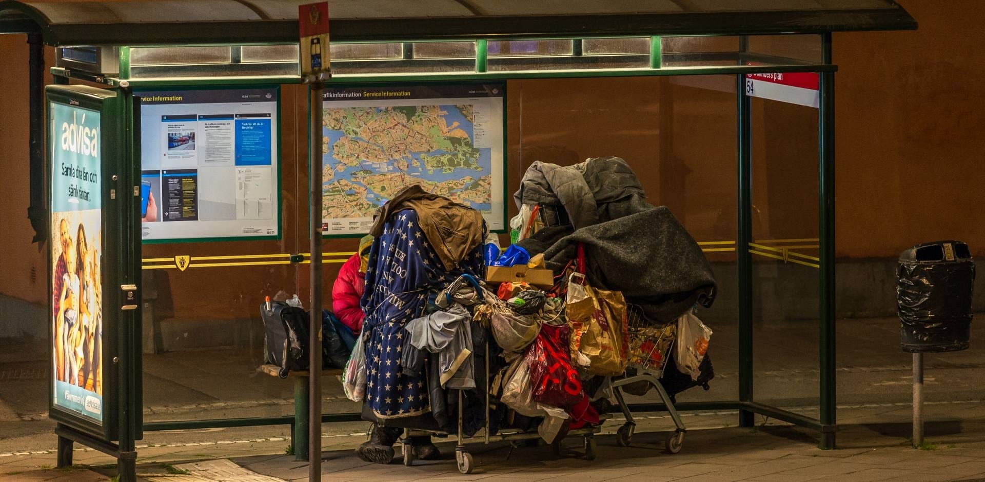 Hemlös med sina tillhörigheter på en busshållplats i Stockholm